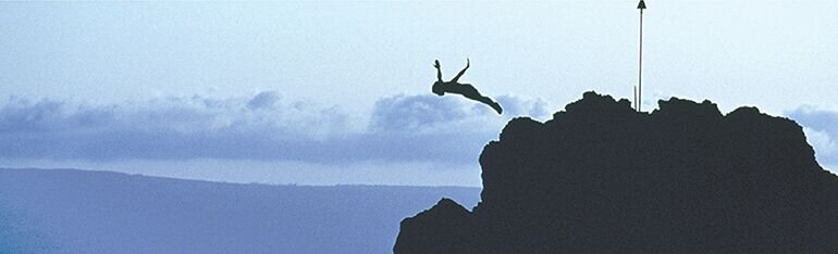 A diver leaps from a dark sea cliff into open sky